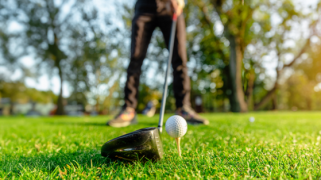 golf ball on tee with golf club and golfer