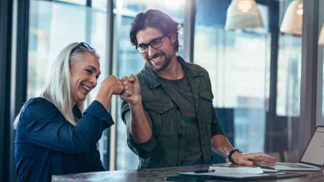 Young businessman and senior businesswoman making a fist bump at office. Business colleagues looking happy and excited after completion of project.