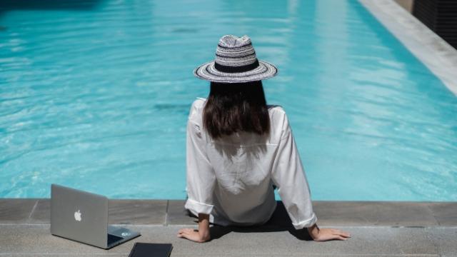 business traveller sitting poolside with laptop