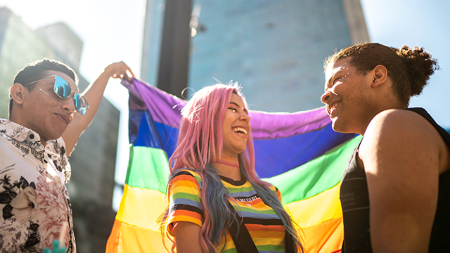 three friends holding a pride flag and laughing