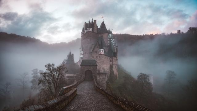 Haunted castle-style house on a hill with fog surrounding it