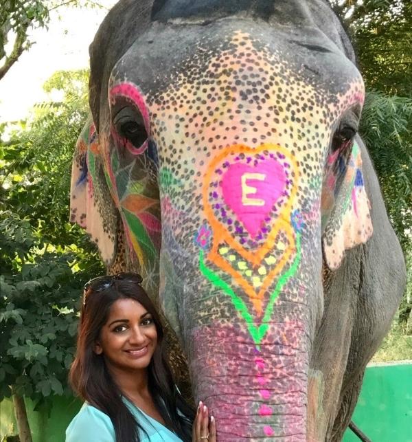 woman standing beside an Asian elephant with a colourful painted "E"