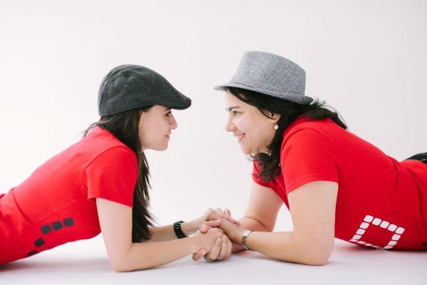 two women wearing red shirts face to face holding hands