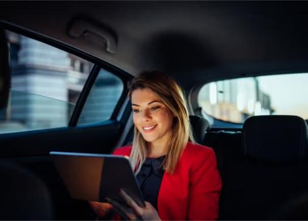 A woman sitting in the backseat of a car holding a tablet representing the sharing economy trend.