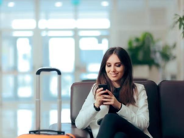 Woman sitting in the airport while looking at smartphone demonstrating how to manage travel loyalty programmes at work.