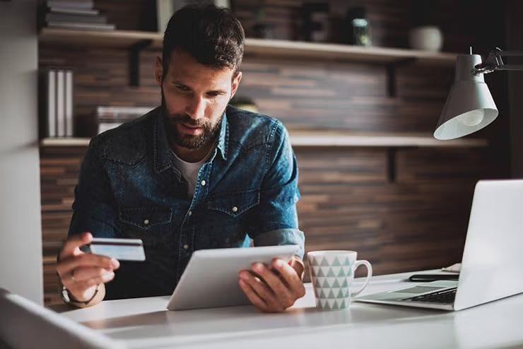 Man holding a credit card and tablet demonstrating tactics for beating travel cost blowout.