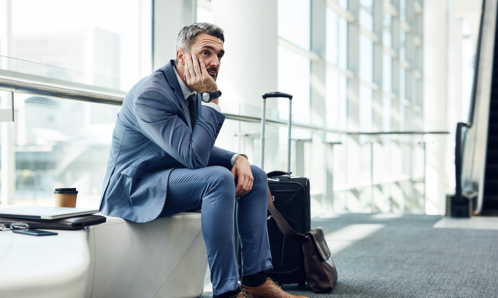 frustrated man sitting at the airport with luggage after travel issues