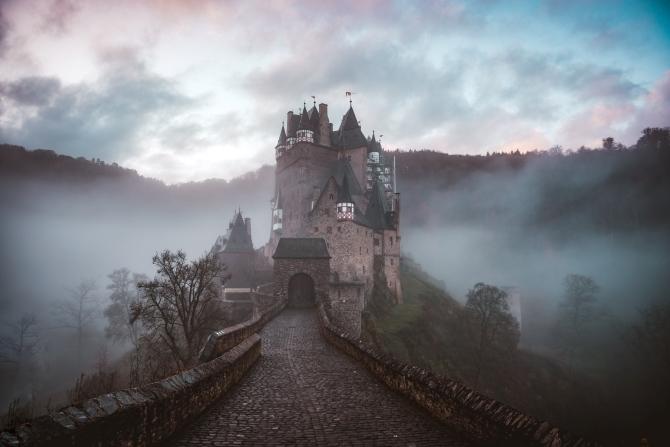 Haunted castle-style house on a hill with fog surrounding it